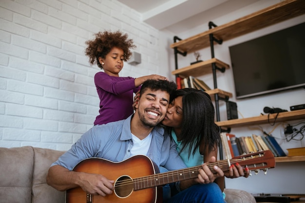 Aufnahme eines jungen Vaters, der Gitarre spielt und von seiner Frau auf die Wange geküsst wird