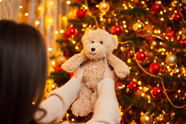 Aufnahme eines Mädchens, das einen Teddybären in der Nähe des Weihnachtsbaums hält Feiert das Weihnachtskonzept, das einen Teddybären als Geschenk erhält