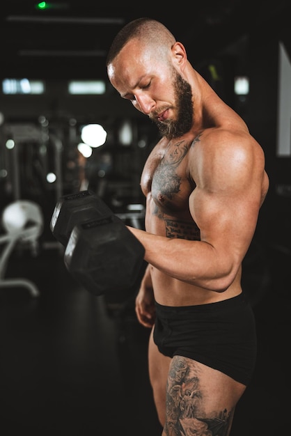 Aufnahme eines muskulösen Bodybuilders, der im Fitnessstudio hart mit Hanteln trainiert. Er pumpt seinen Bizepsmuskel mit schwerem Gewicht auf.