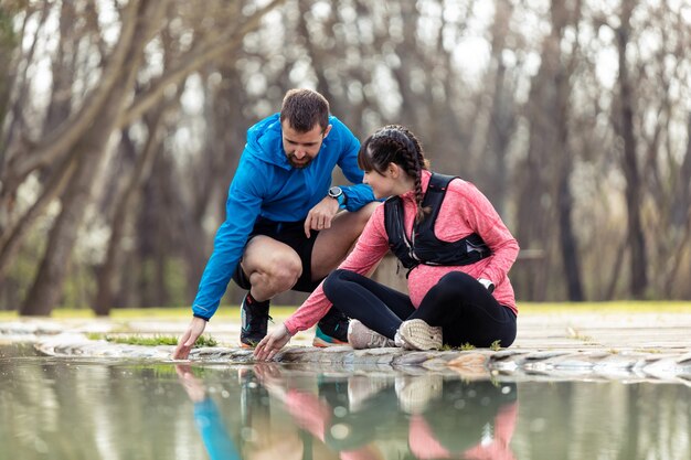 Aufnahme eines sportlichen jungen Paares, das mit dem Wasser im Teich spielt und die gemeinsame Zeit im Freien genießt.