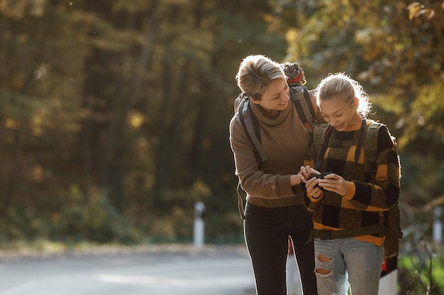 Aufnahme eines Teenager-Mädchens und ihrer Mutter mit digitaler Fotokamera beim gemeinsamen Spaziergang durch den Wald im Herbst.