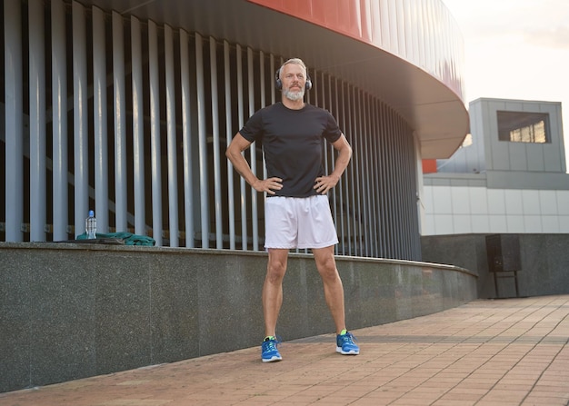 Aufnahme in voller Länge eines aktiven Sportlers mittleren Alters in Sportbekleidung und Kopfhörern, die sich aufwärmen