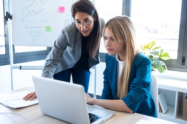 Aufnahme von zwei Geschäftsfrauen, die mit Laptop im Büro zusammenarbeiten.