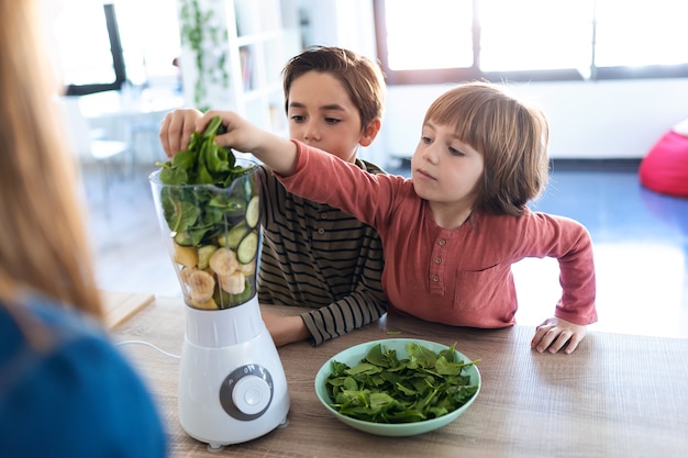 Aufnahme von zwei Jungen, die seiner Mutter helfen, einen Detox-Saft mit einem Mixer in der Küche zu Hause zuzubereiten.