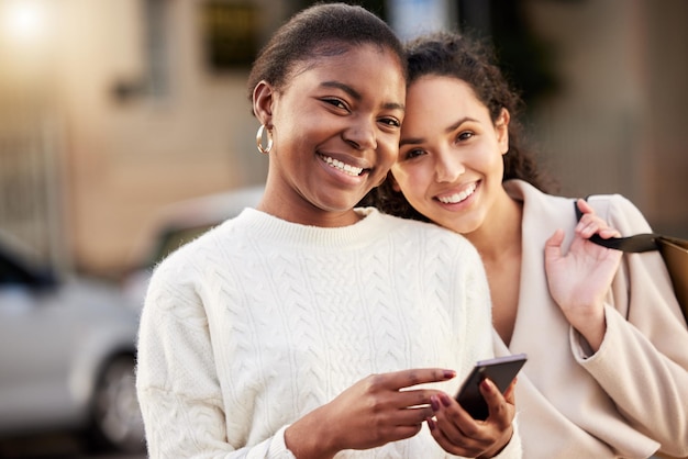 Aufnahme von zwei jungen Frauen, die ein Smartphone beim Einkaufen vor einem urbanen Hintergrund benutzen