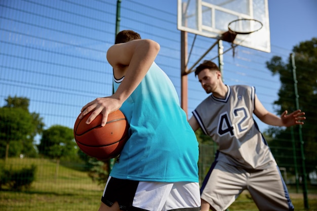 Aufnahme von zwei Männern, die Basketball spielen. Fokus auf den Ball in der Hand, der sich auf den Pass vorbereitet