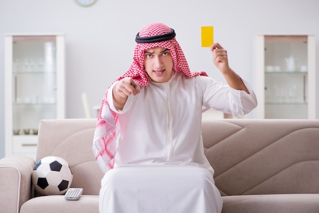 Aufpassender Fußball des jungen arabischen Mannes, der auf Sofa sitzt