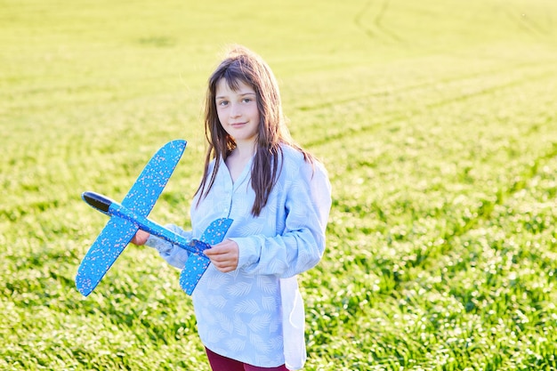 Aufrichtige Emotionen Fröhliches kleines Mädchen, das mit blauem Spielzeugflugzeug in den Händen auf dem Feld läuft