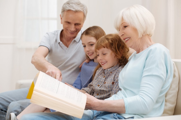 Aufrichtige erfinderische erstaunliche frau, die ihr lieblingsbuch mit kindern teilt, die sie und opa am wochenende besuchen