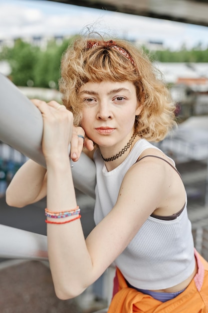 Foto aufrichtiges porträt einer jungen frau mit lockigem haar, die im freien in die kamera schaut und trendiges outfit trägt