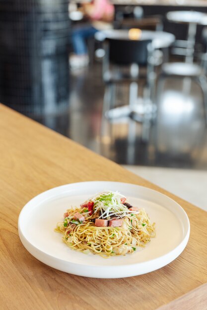 Aufruhr briet chinesische Nudel mit Schinken- und Krebsfleisch auf Holztisch mit Unschärfehintergrund.