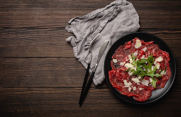 Aufschnitt Vorspeise Rindercarpaccio mit Parmesan-Käse und Arugula auf schwarzem Teller