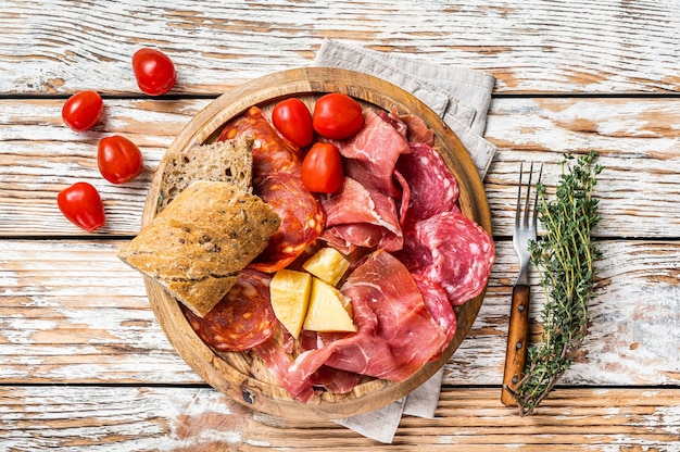 Aufschnittplatte, traditionelle spanische Tapas der Wurstwaren auf einem Holzbrett. Weißer hölzerner Hintergrund. Ansicht von oben.