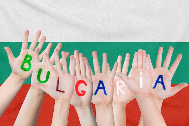 Aufschrift Bulgarien auf den Händen der Kinder gegen die Oberfläche einer wehenden Flagge der Bulgarien