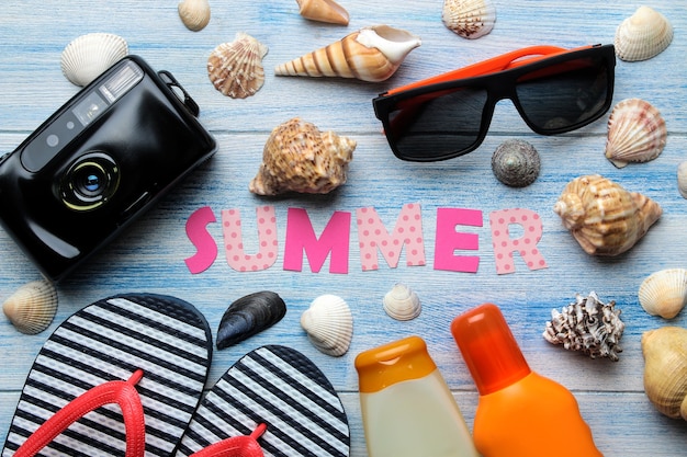 Aufschrift Sommer aus Papier mit bunten Buchstaben und Muscheln und Sommer- und Meereszubehör auf einem blauen Holztisch. Sommer. Entspannung. Ferien. Ansicht von oben
