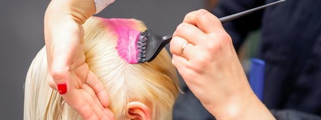 Auftragen von rosa Farbstoff mit dem Pinsel auf das weiße Haar einer jungen blonden Frau in einem Friseursalon