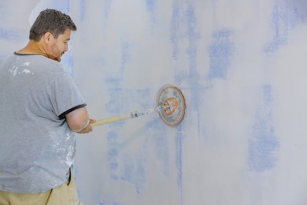 Auftragnehmer mit Sandkelle schleifen die Trockenbauwand an der Wand