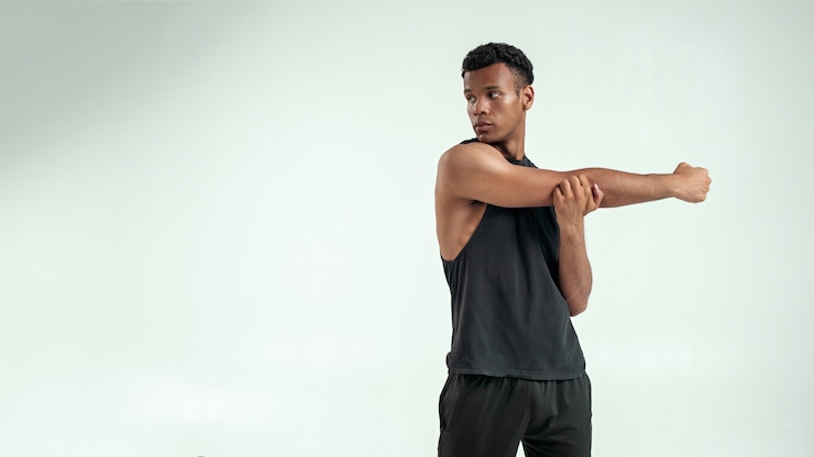 Foto aufwärmen starker junger afroamerikanischer mann, der seinen arm ausdehnt, während er vor grauem hintergrund steht