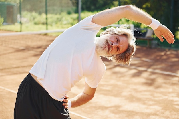 Foto aufwärmübungen machen älterer, moderner, stylischer mann im freien auf dem sportlichen feld tagsüber