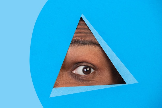 Auge des afroamerikanischen Mannes, der durch das Dreieck im blauen Hintergrund späht