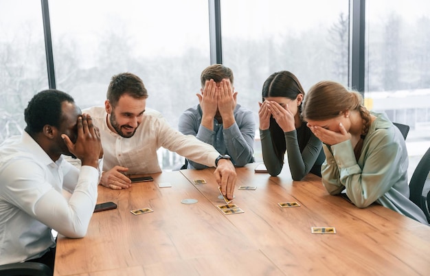 Augen mit den Händen bedecken, Kartenspiel spielen, ein Team von Büroangestellten ist im Innenraum zusammen.