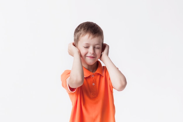 Augen schlossen den lächelnden Jungen, der seine Ohren mit der Hand gegen weißen Hintergrund bedeckt