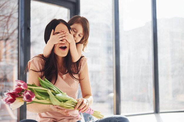 Augen zudecken Tochter gratuliert Mutter zum Urlaub und gibt Blumenstrauß