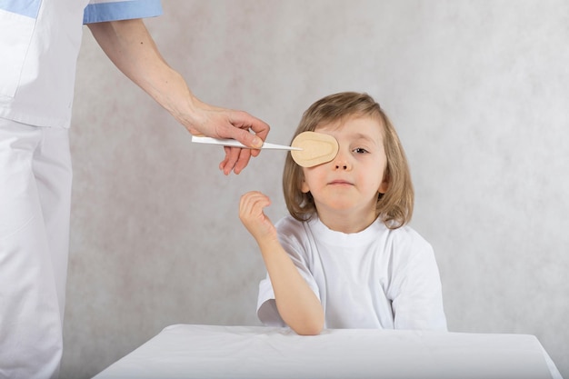 Augenarzt schließt die Augen des Jungen mit Augenpad. Grauer Hintergrund