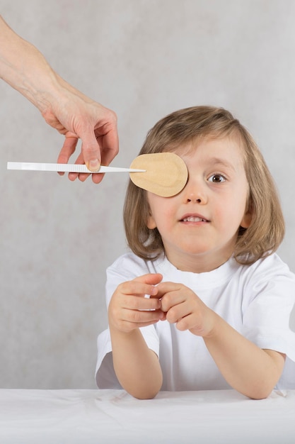 Augenarzt schließt die Augen des Jungen mit dem Augenpad falsch. Grauer Hintergrund