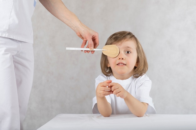 Augenarzt schließt die Augen des Jungen mit dem Augenpad falsch. Grauer Hintergrund