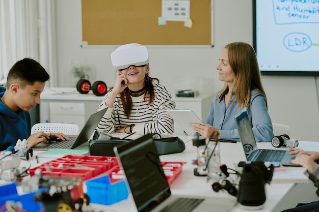 Aula de ciencias de la computación con niños codificando a través de computadora portátil chica con camisa a rayas disfrutando de auriculares VR y