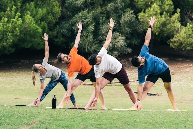 Aula com quatro pessoas fazendo a pose do triângulo de ioga em um parque