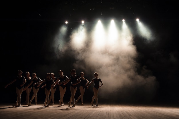 Aula de balé no palco do teatro com luz e fumaça. as crianças estão envolvidas em exercícios clássicos no palco.