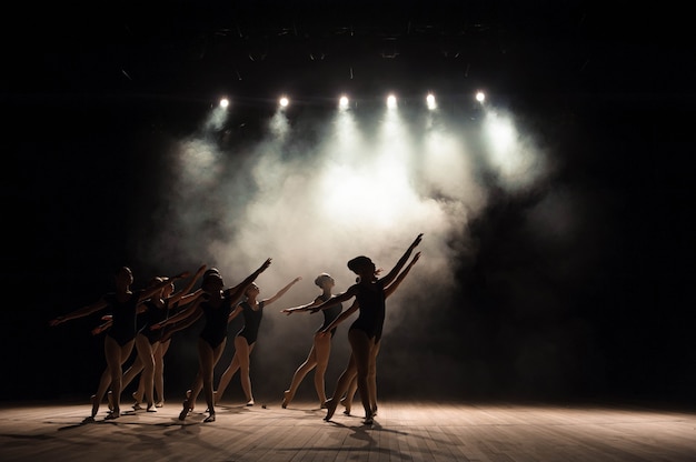 Aula de balé no palco do teatro com luz e fumaça. as crianças estão envolvidas em exercícios clássicos no palco.