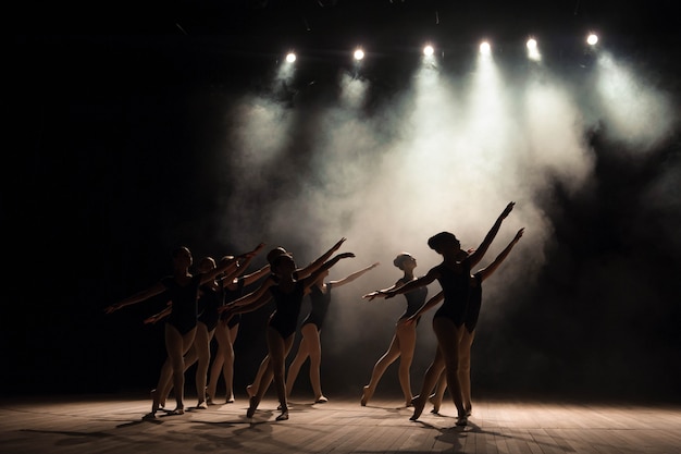 Foto aula de balé no palco do teatro com luz e fumaça.