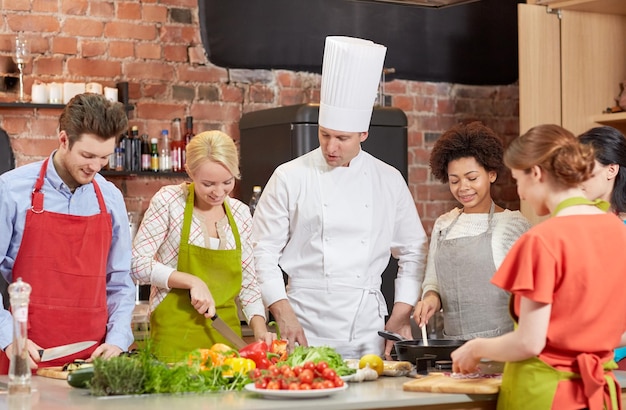 aula de culinária, culinária, comida e conceito de pessoas - feliz grupo de amigos e chef masculino cozinhando na cozinha