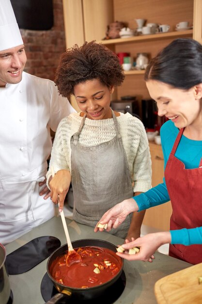 aula de culinária, culinária, comida e conceito de pessoas - feliz grupo de mulheres e chef masculino cozinhando molho de tomate na cozinha