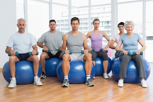 Aula de fitness com halteres sentados em bolas de ginástica na academia