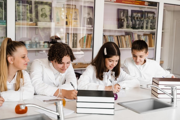 Aula de química em laboratório na escola Alunos escrevendo lição de casa sorrindo e se divertindo juntos no laboratório da escola