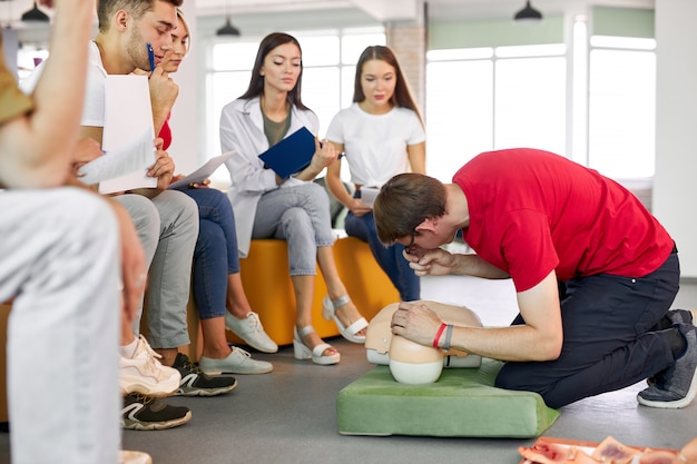 Aula de RCP com jovens instrutores caucasianos falando e demonstrando os primeiros socorros de ajuda