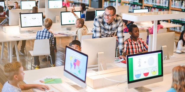 Aula diversa con niños que usan computadoras El maestro ayuda a los estudiantes Los niños aprenden con tecnología Niños involucrados en un entorno educativo moderno Estudiantes internacionales que trabajan con computadoras