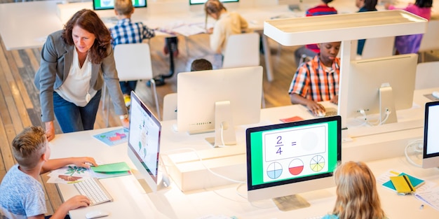 Aula con niños diversos que usan computadoras El maestro ayuda a los estudiantes Los niños aprenden con tecnología Un entorno educativo brillante y atractivo El maestro enseña a los estudiantes jóvenes