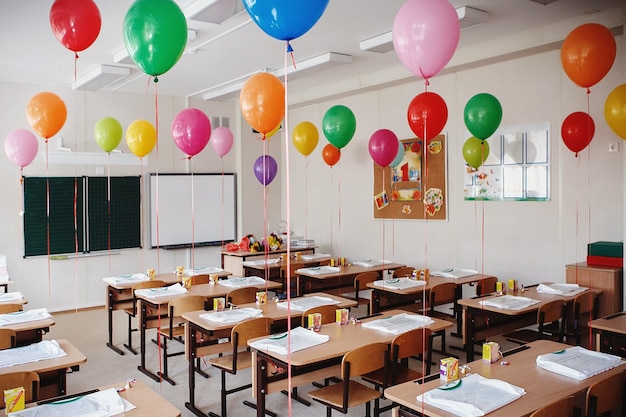 Aula con pupitres y pizarra decorada con globos de colores
