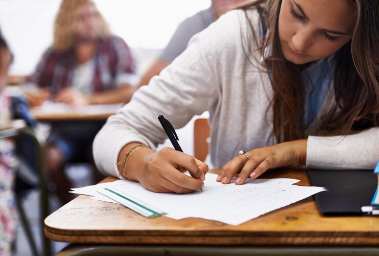 Foto aula universitaria y mujer escribiendo examen en el escritorio para el conocimiento de la educación y la oportunidad de aprendizaje universitario y estudiante con papel para la evaluación de la prueba y estudiar con libros notas o informe