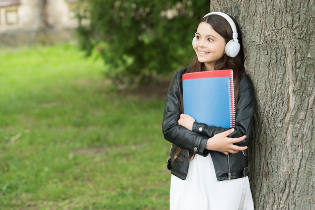 Aulas de escuta Menina feliz pratica habilidades de escuta ao ar livre Criança gosta de ouvir música Curso de escuta Aprendizagem à distância Estudo e educação Vida moderna Escola de idiomas