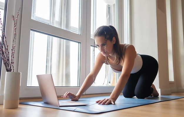 Aulas de ioga online Garota de ioga positiva fazendo prática matinal na frente do laptop em casa