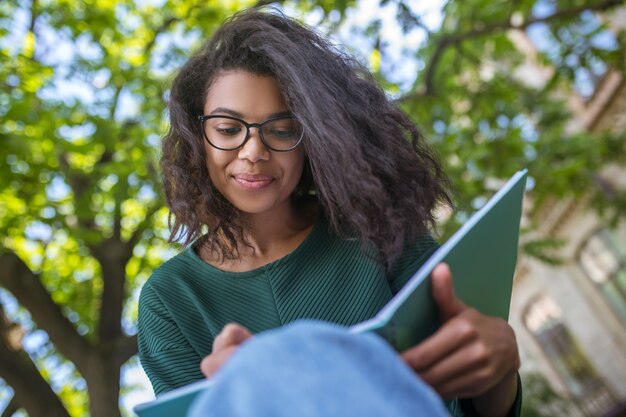 Aulas. Uma garota de cabelos escuros usando óculos escrevendo algo em um caderno