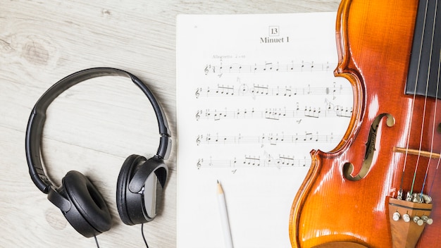 Foto auricular; lápiz; y violín sobre nota musical sobre fondo de madera