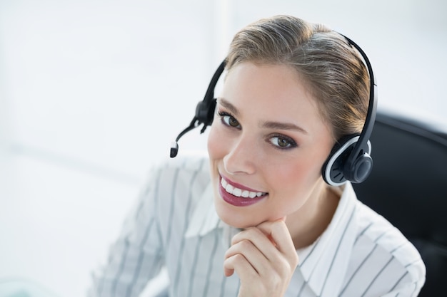 Auricular que lleva sonriente hermoso del agente que se sienta en su escritorio