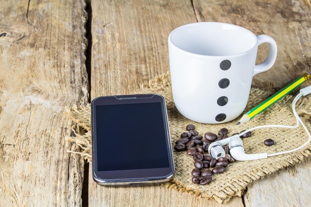 Auricular de teléfono inteligente granos de café y taza de café en la mesa de madera